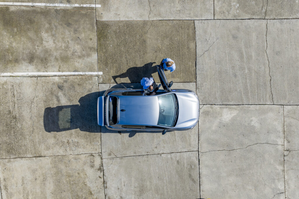 Férias sem preocupações com caução e seguros. Vista aérea de um carro alugado com a Neblu, no seu espaço comercial, acompanhado pelos profissionais que se asseguram que a viatura tem todas as condições necessárias para alcançar o seu objetivo: passear.
